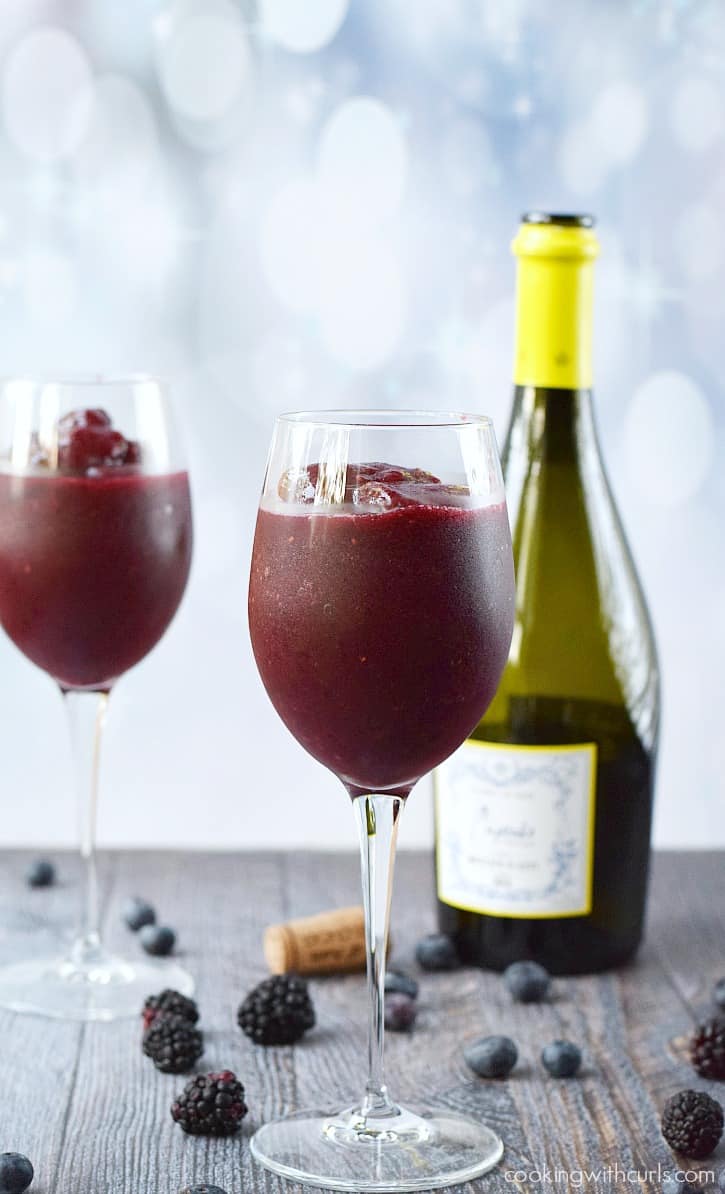 Blended berries and wine in two wine glasses surrounded by blackberries with a bottle of wine in the background..