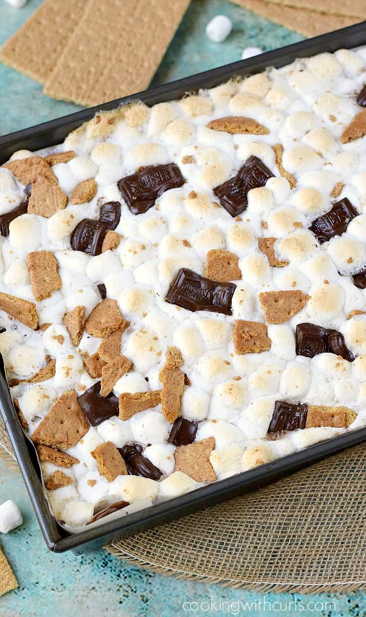 A pan of smores brownies topped with melted mini marshmallows, chocolate bars and graham cracker pieces.