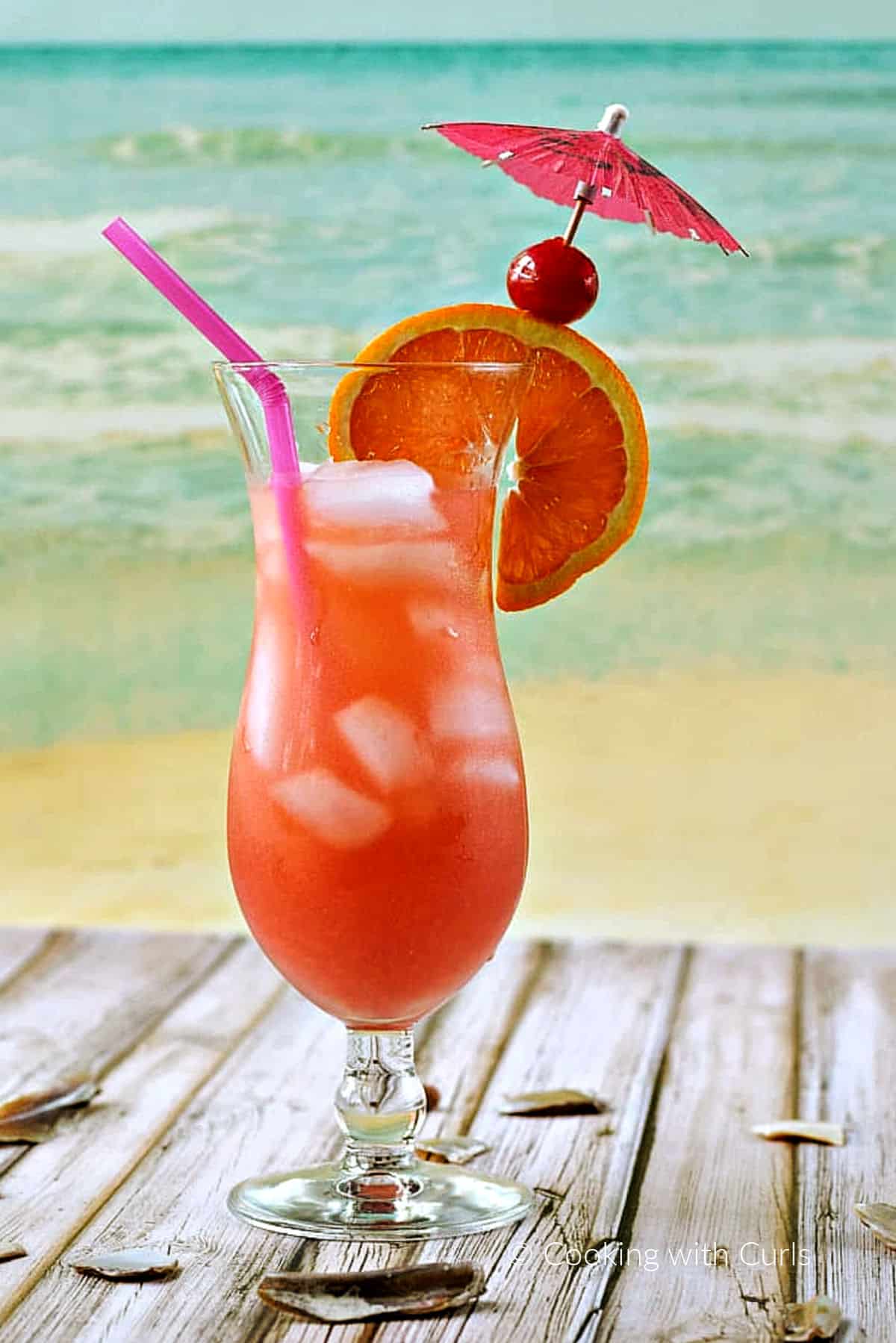 A bright pink Bahama Mama drink in a hurricane glass garnished with an orange wheel, cherry, and pink paper umbrella.