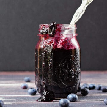 Blueberry preserves in a glass mason jar with a spoon sticking out of the top.