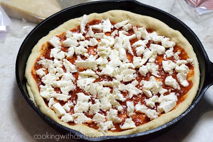 Pizza dough topped with tomato sauce and mozzarella cheese in a cast iron skillet.