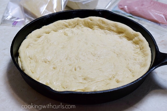 Pizza dough pushed up the sides of  a cast iron skillet.