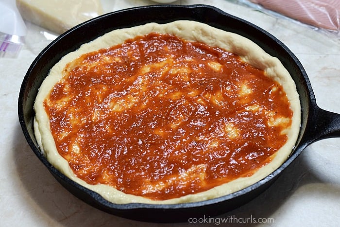 Pizza dough topped with tomato sauce in a cast iron skillet.