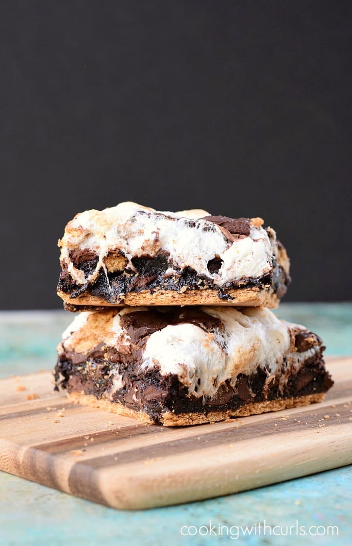Two smores brownies stacked on a wood cutting board.