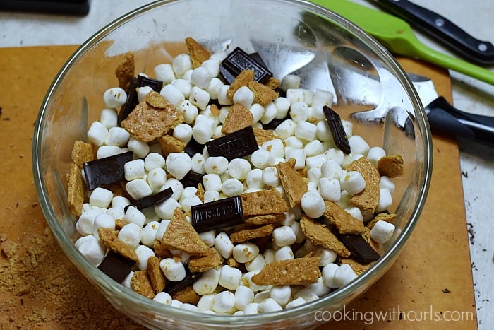 Mini marshmallows, pieces of hershey's chocolate bars, and broken graham cracker pieces tossed with melted butter in a large glass bowl.