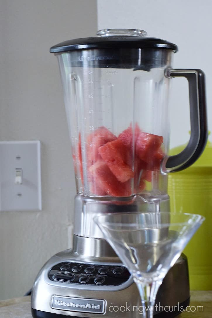 Frozen watermelon chunks in a blender behind an empty margarita glass.