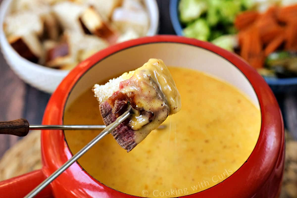 Bread cube with bacon and steak on a fondue fork dipped into cheese fondue.