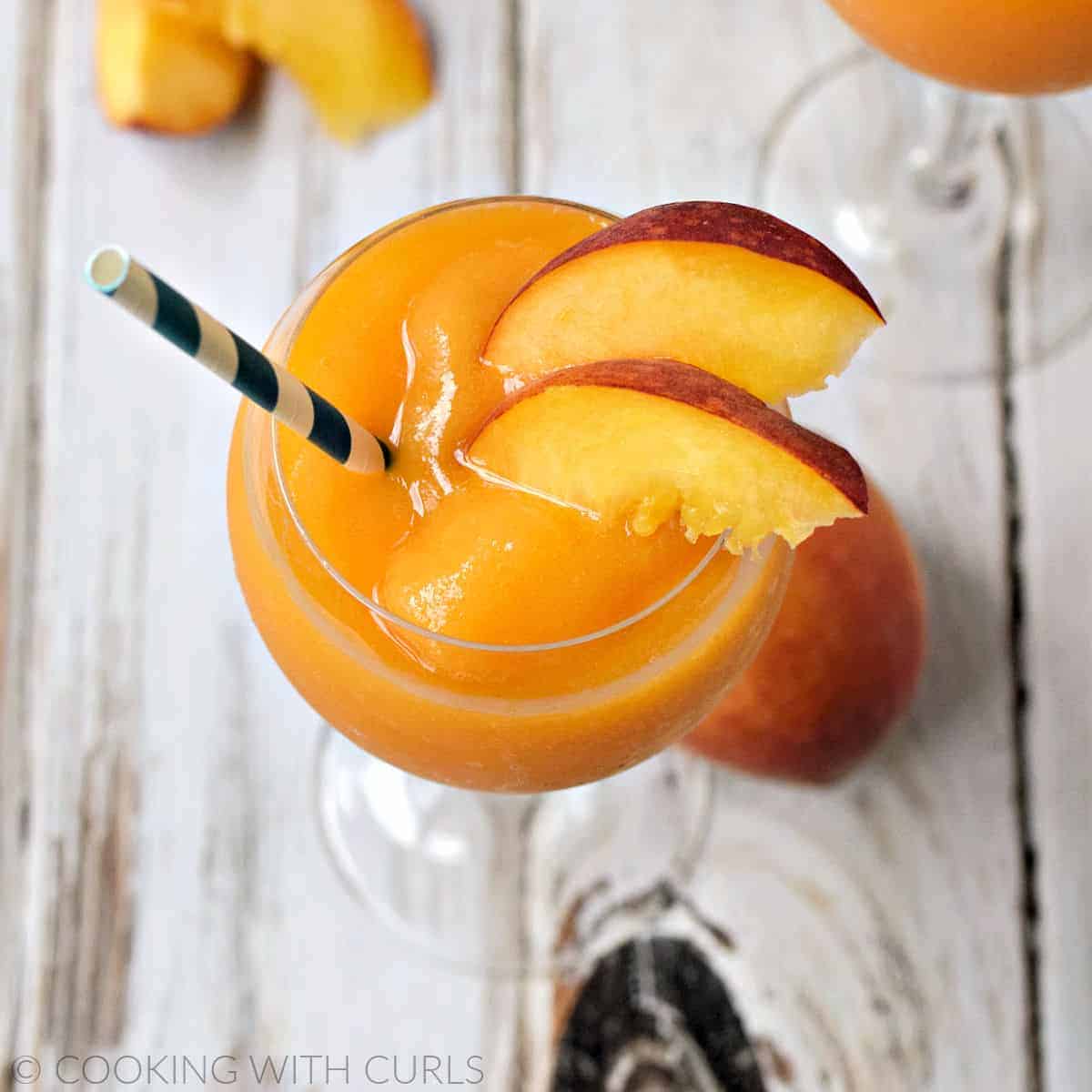 Looking down on two wine glasses filled with blended peaches and wine smoothie garnished with peach slices.