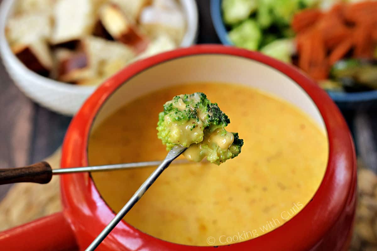 Steamed broccoli floret on a fondue fork dipped into cheese fondue with beer.