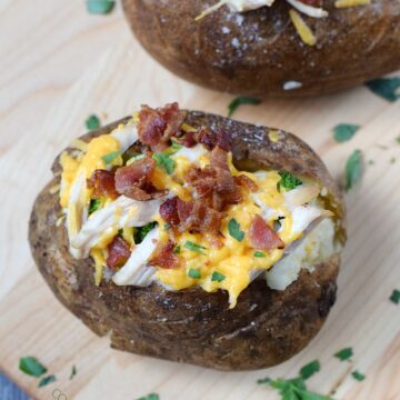 Two Stuffed Baked Potatoes sitting on a wooden cutting board.