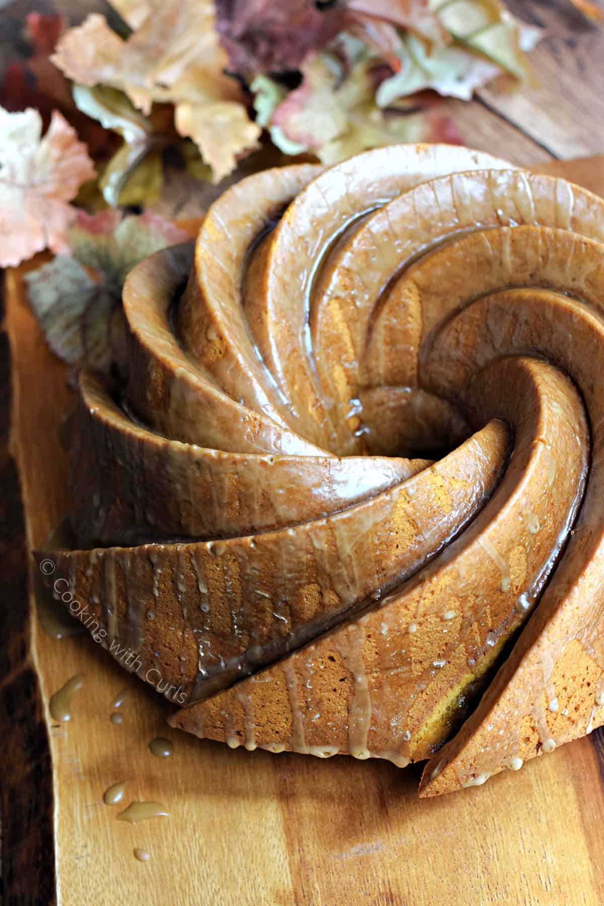 A swirl patterned bundt cake with glaze dripping down the sides sitting on a wood serving board.
