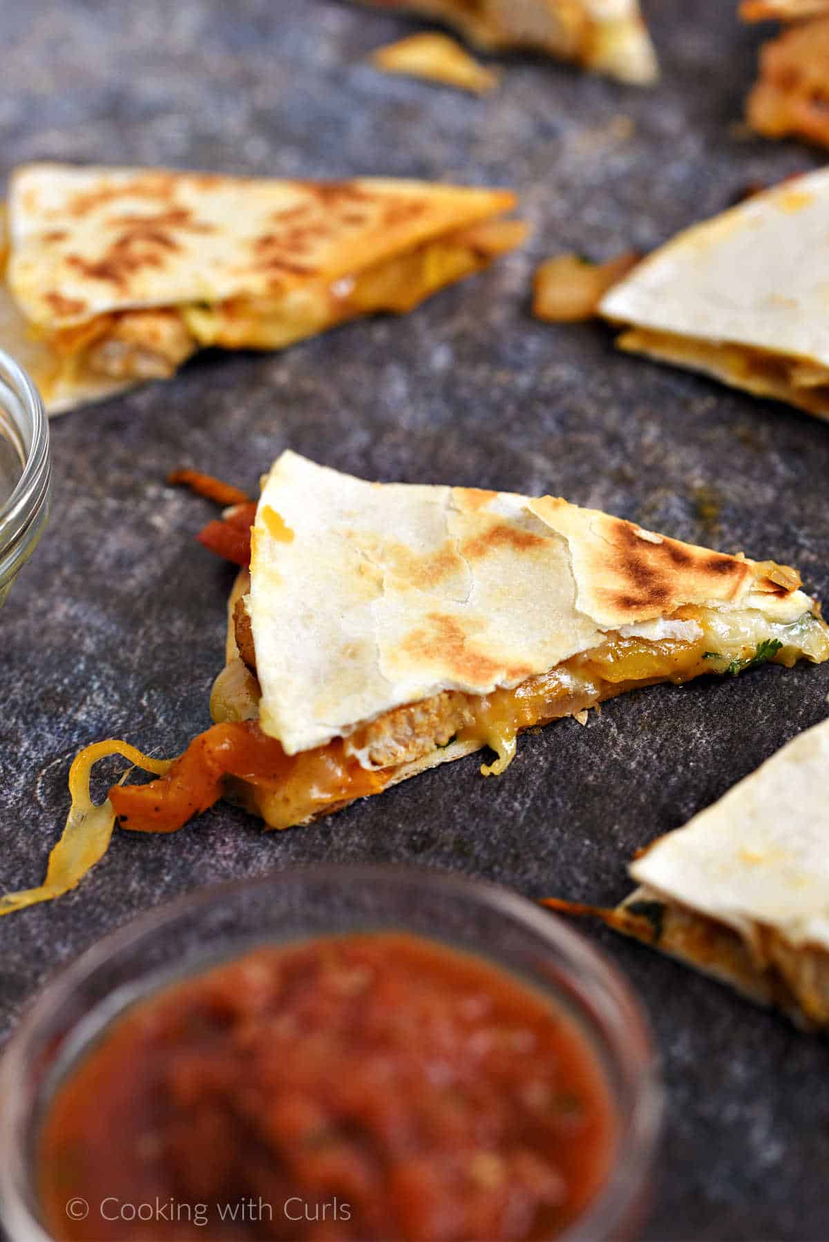 Cheesy chicken fajita quesadilla wedges spread out on a board with a bowl of salsa.