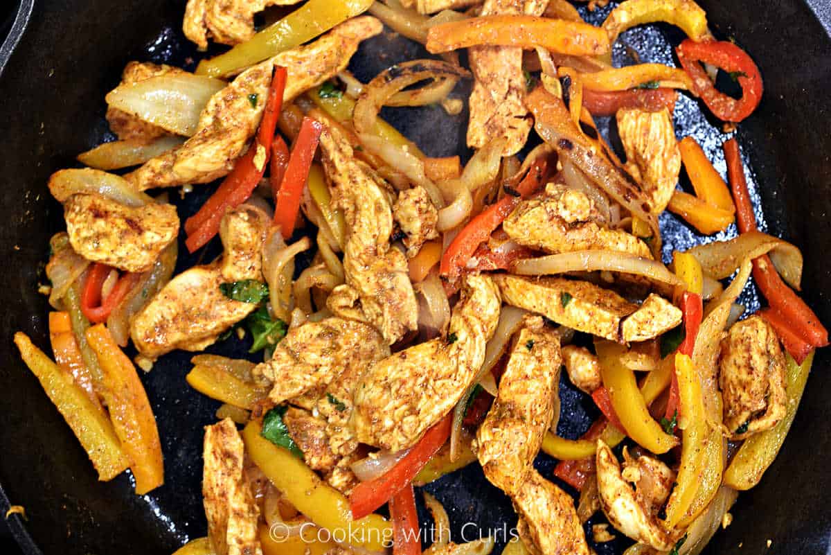 Chicken fajitas cooking in a cast iron skillet.