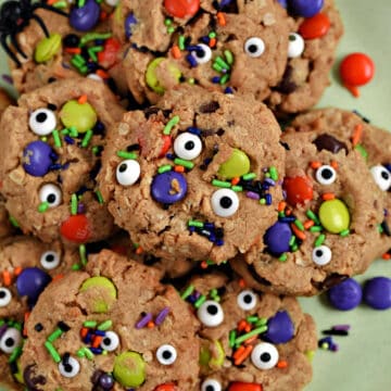 Cookies topped with candy eyes, M&M's, and colorful sprinkles piled up on a green plate.