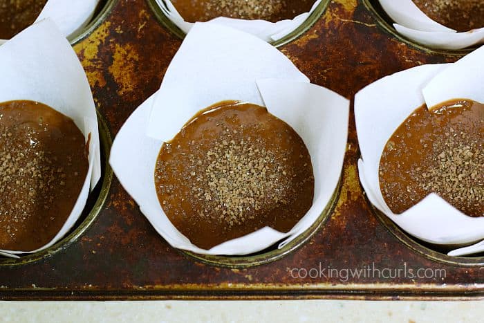 Sugar crystals on top of six mocha muffins in white paper liners inside a muffin tin.