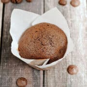 Chocolate muffin in white paper liner surrounded by coffee beans and dark chocolate chips.