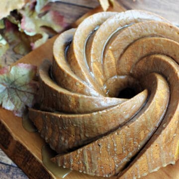 A swirled patterned bundt cake drizzled with glaze on a wood serving board.