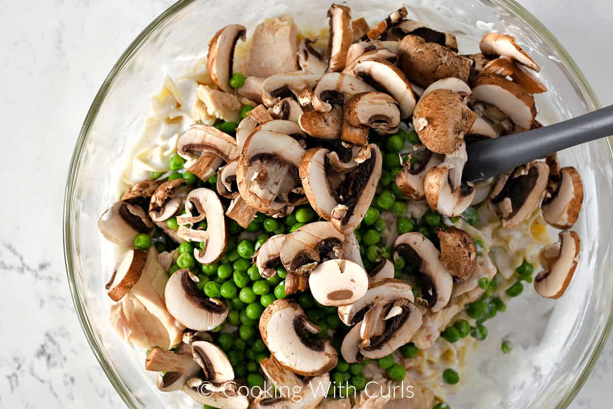 Sliced mushrooms on peas, on top of the sauce and noodle mixture in a large bowl. 