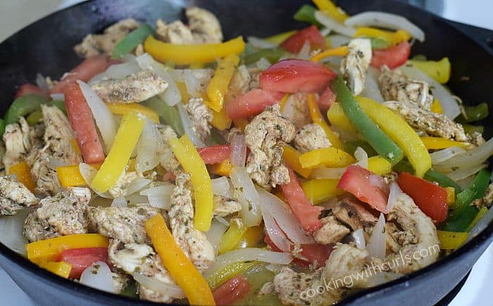Strips of chicken, onion, and bell peppers in a cast iron skillet.