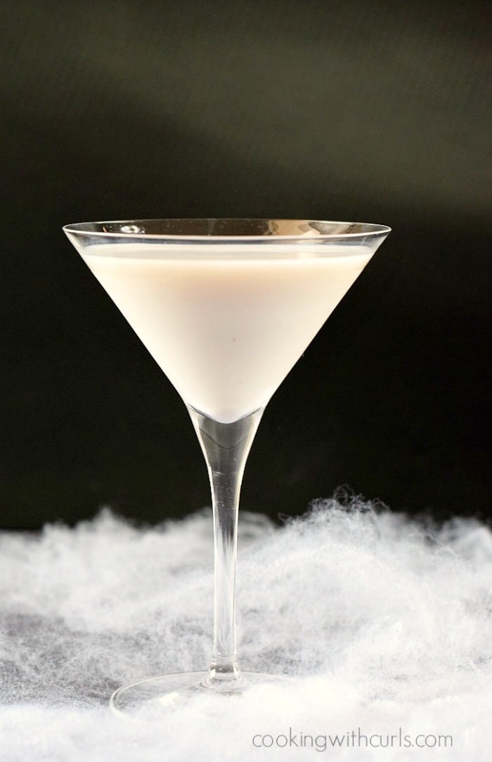 Liquefied Ghost Martini in a martini glass surrounded by fake spider webs with a black background.