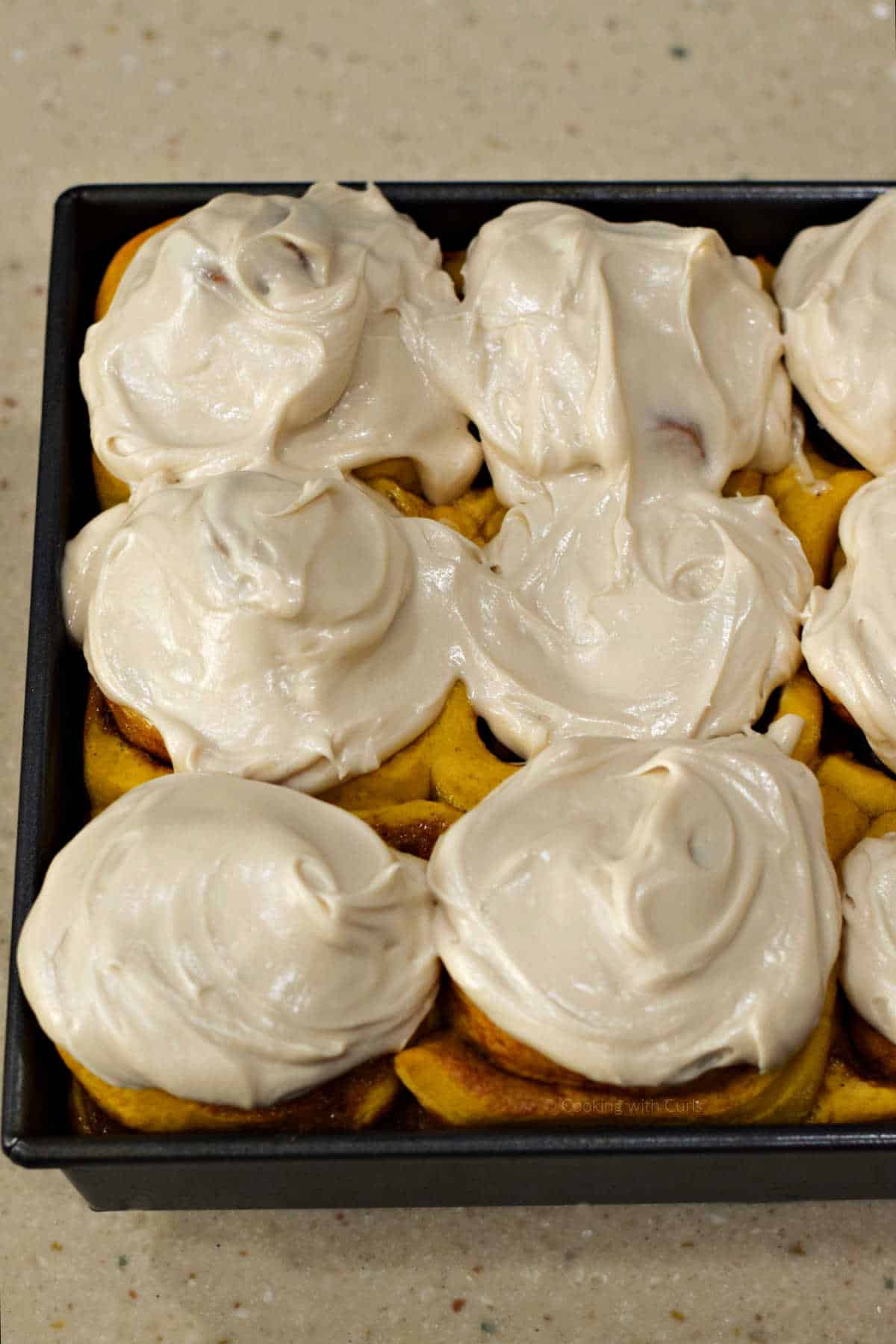 Pumpkin cinnamon rolls in baking pan topped with maple cream cheese frosting.