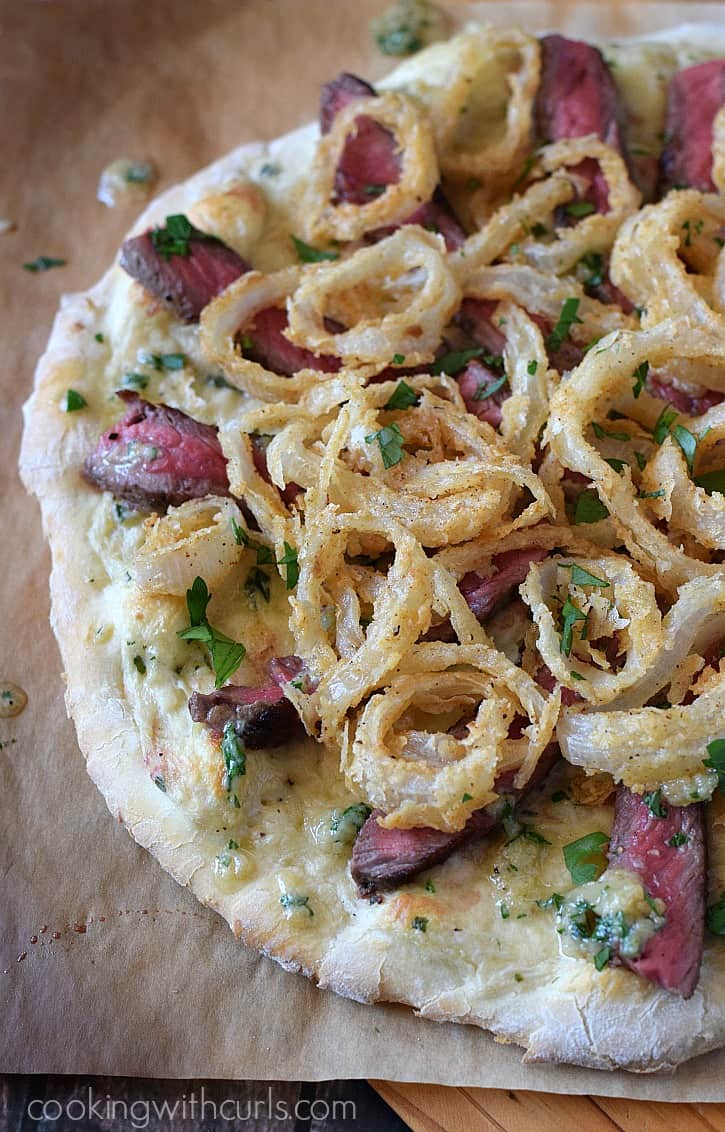 Steakhouse Pizza  topped with white pizza sauce, medium-rare steak, Gorgonzola butter, and crispy onion rings. 