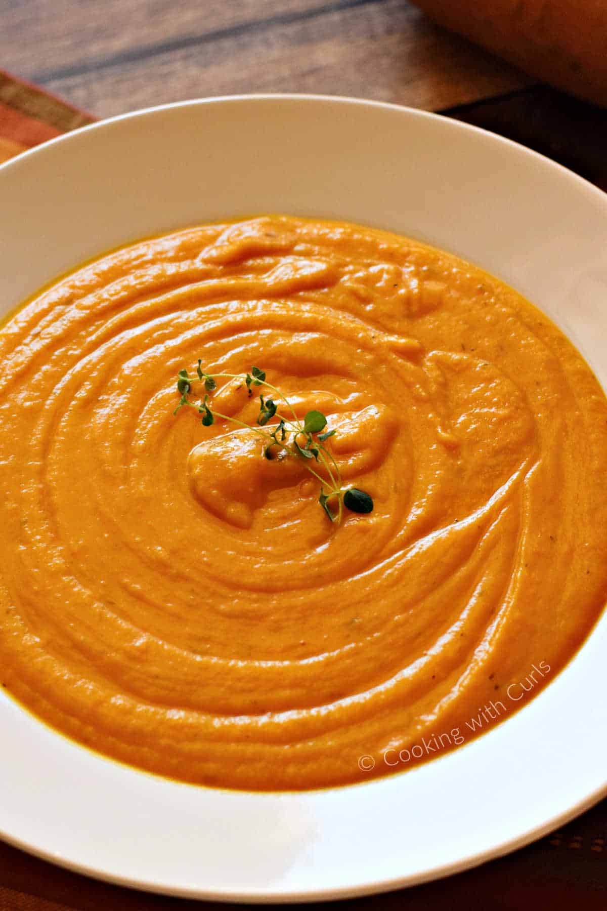 A bowl of creamy roasted sweet potato soup with fresh thyme sprigs in the center.