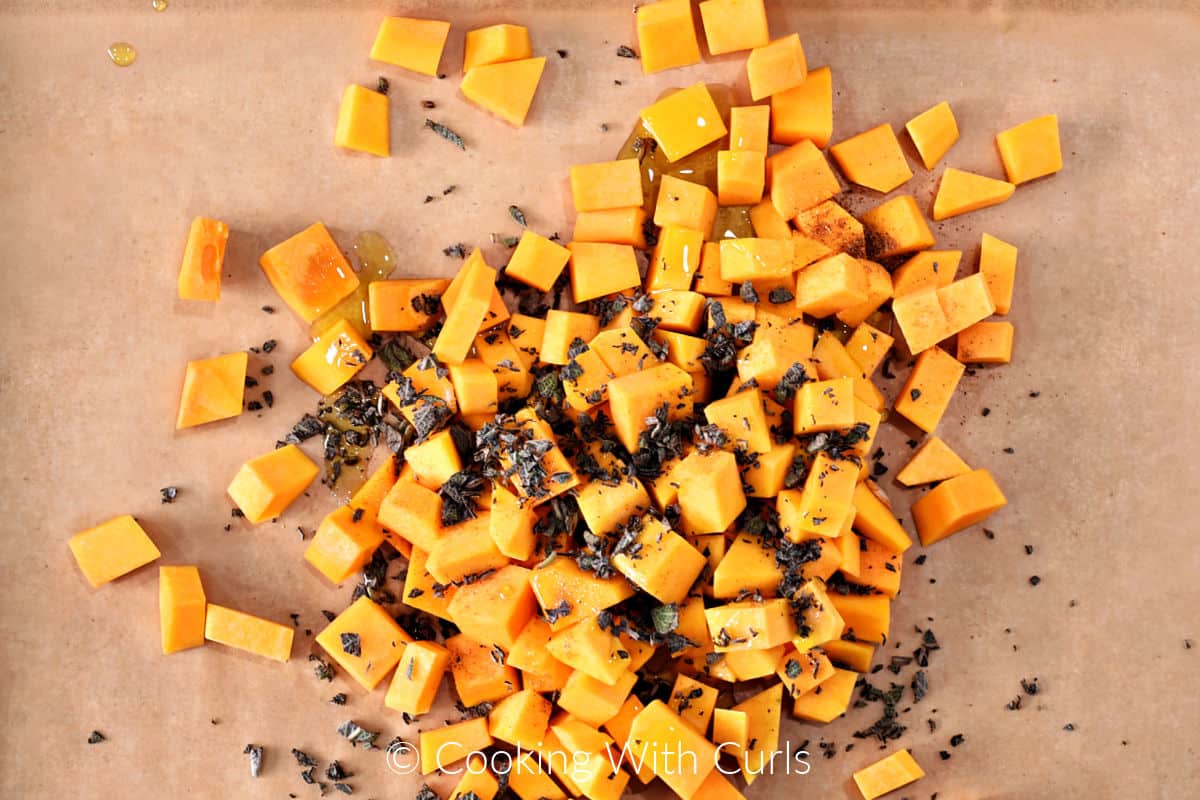 Butternut squash cubes, oil, and chopped sage on a parchment lined baking sheet. 