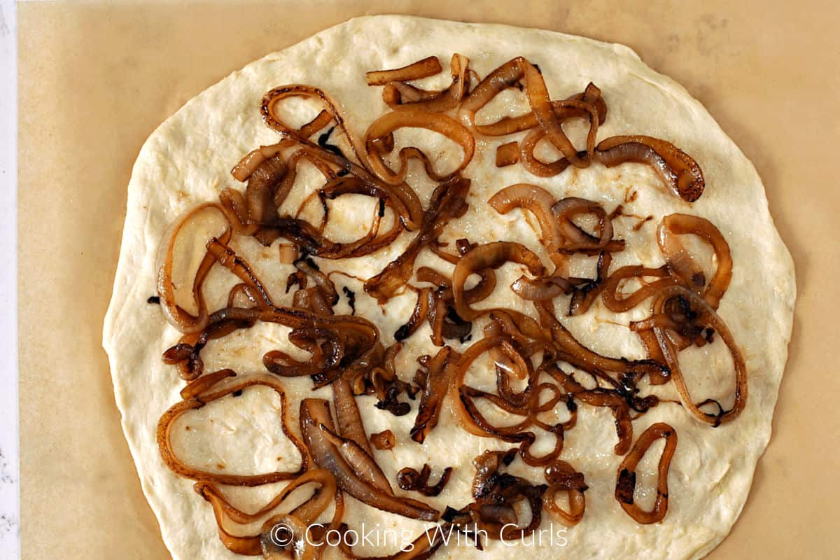 Caramelized onions on a pizza dough circle sitting on a sheet of parchment paper. 