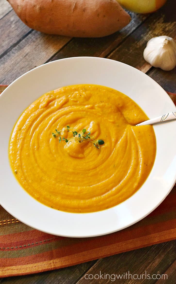 a big white bowl of creamy roasted sweet potato soup with sweet potatoes in the background