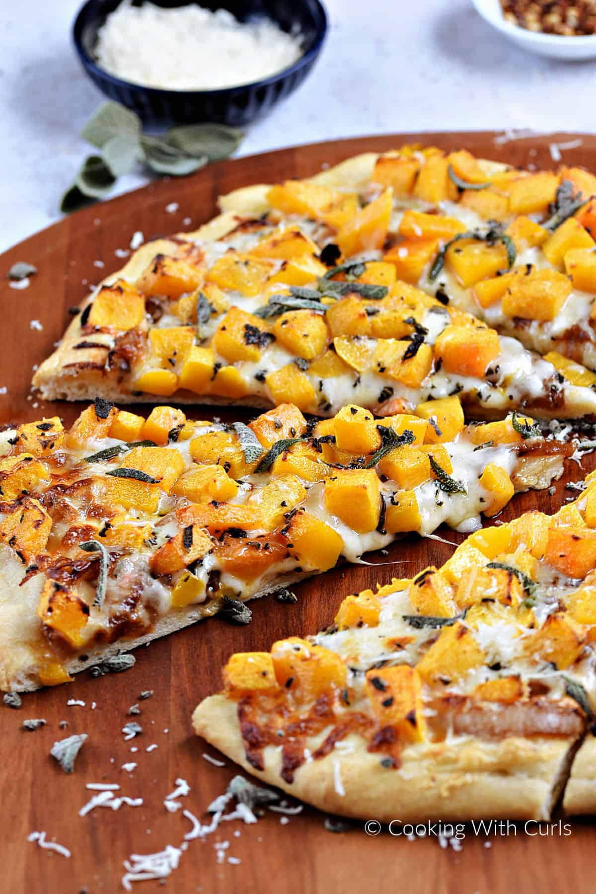 Four slices of pizza topped with melted cheese, butternut squash cubes, and fresh sage on a wooden pizza peel. 