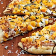 Four slices of pizza topped with melted cheese, butternut squash cubes, and fresh sage on a wooden pizza peel.