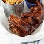 a parchment paper lined basket with barbecue ribs, a pail of potato wedges and a blue ramekin with extra barbecue sauce