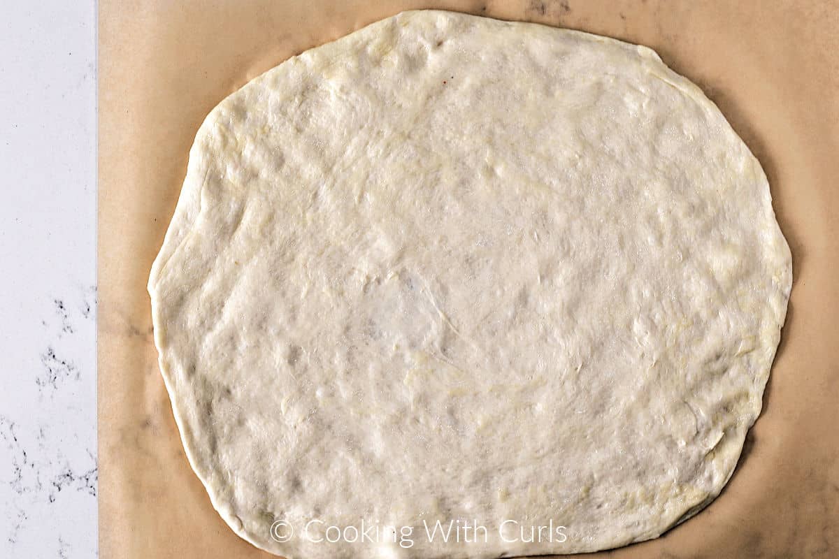 Raw pizza dough circle on a sheet of parchment paper.