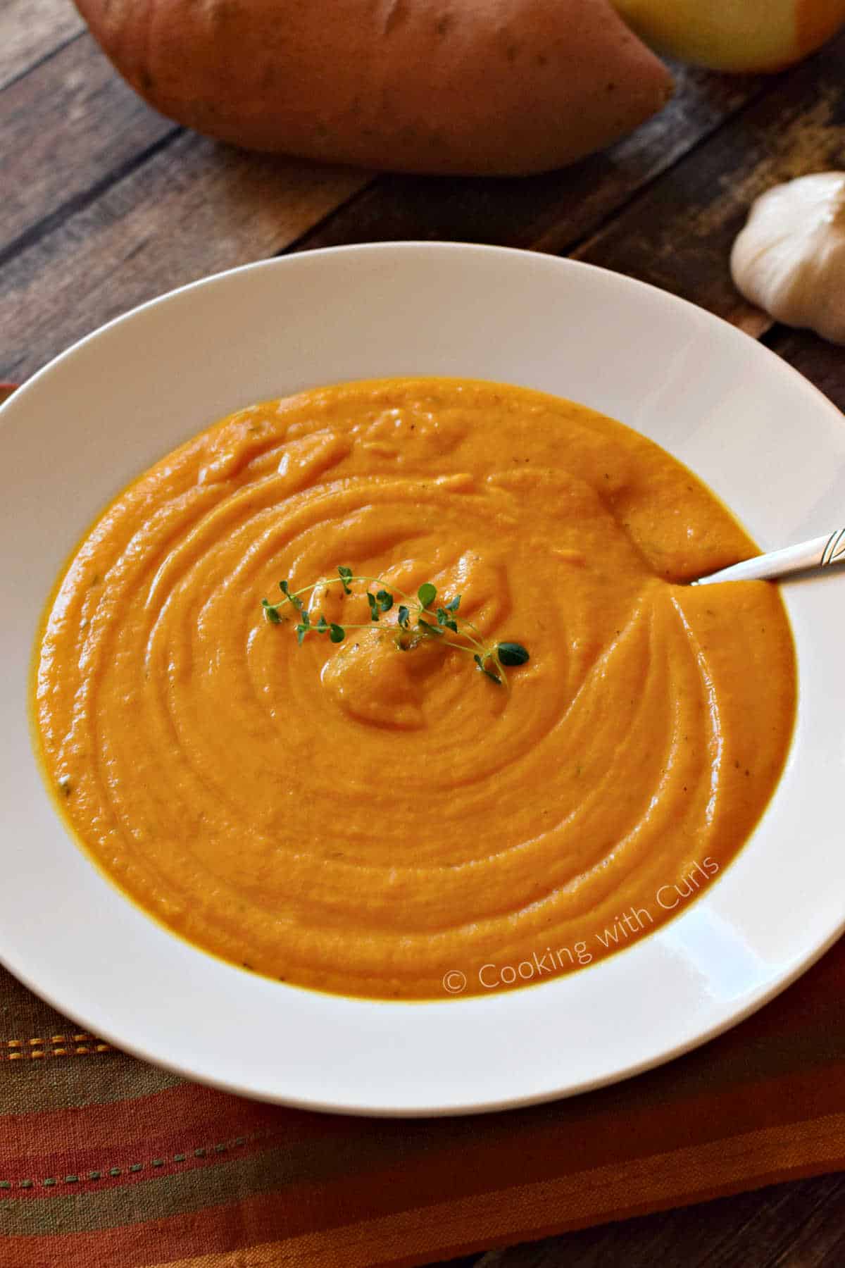 A bowl of creamy roasted sweet potato soup with sweet potatoes in the background.
