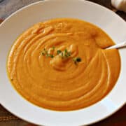 A bowl of creamy roasted sweet potato soup with sweet potatoes in the background.