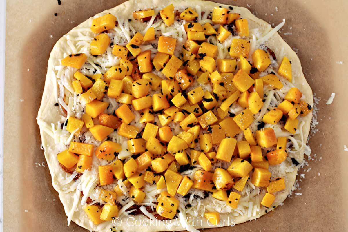 Roasted squash cubes, shredded cheese, and caramelized onions on a pizza dough circle. 