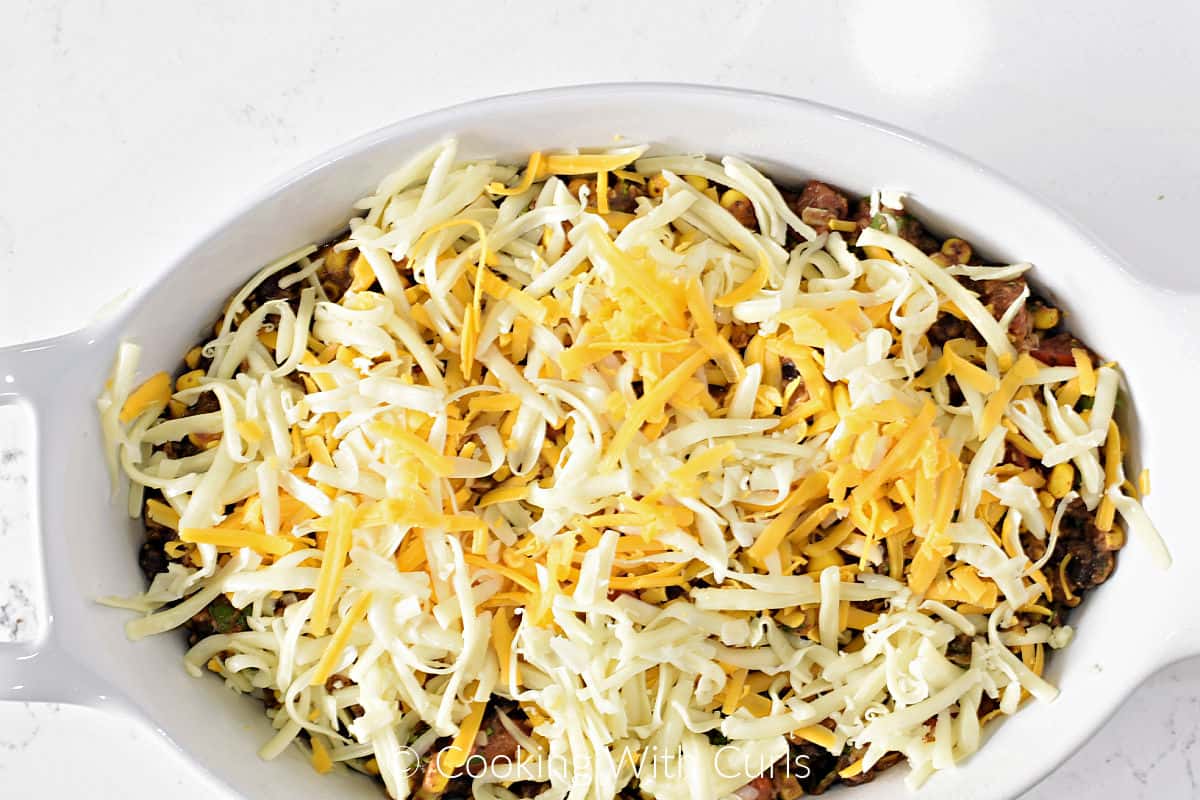 Black bean dip covered in grated cheddar and Jack cheese in an oval baking dish. 