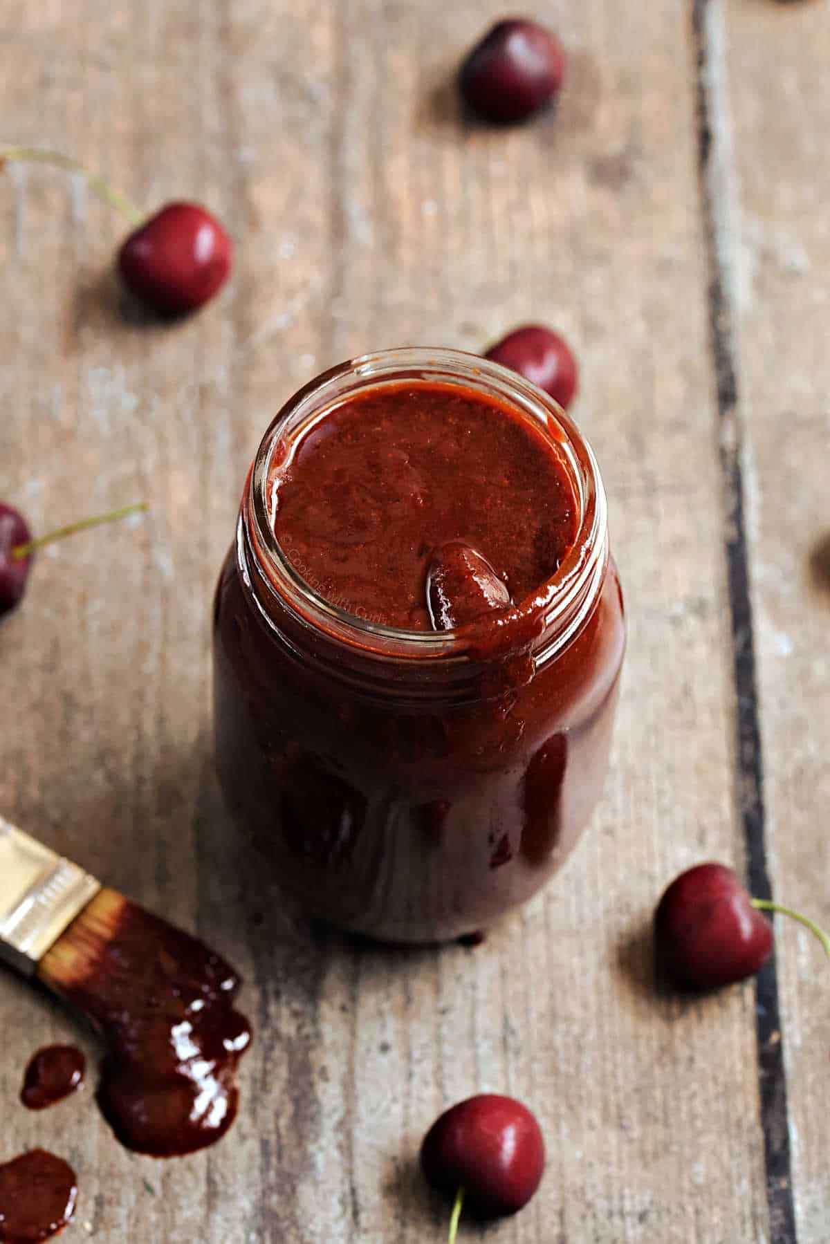 Cherry chipotle bbq sauce in a glass mason jar surrounded by fresh cherries.