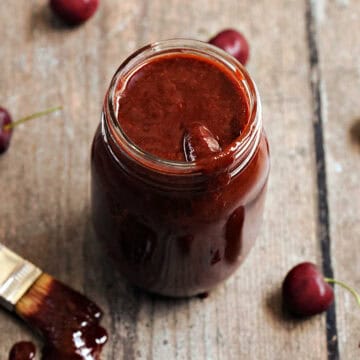 Cherry chipotle bbq sauce in a glass mason jar surrounded by fresh cherries.