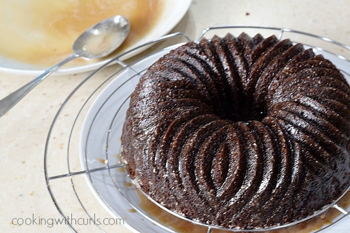 Baked bundt cake on a round, wire cooling rack with glaze poured over the top.