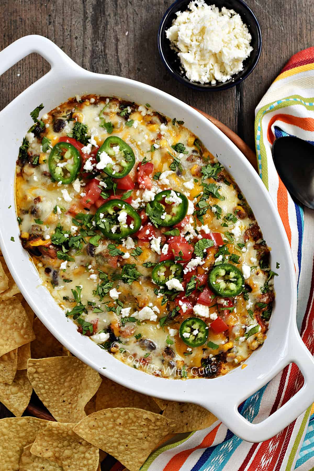 Looking down on an oval baking dish filled with Southwest Black Bean Dip topped with melted cheeses, jalapeno slices, and cilantro. 