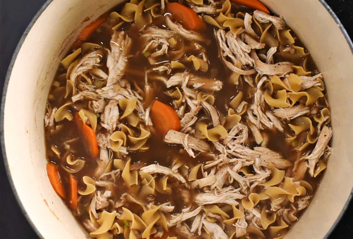 Shredded chicken, sliced carrots and egg noodles in a large pot. 