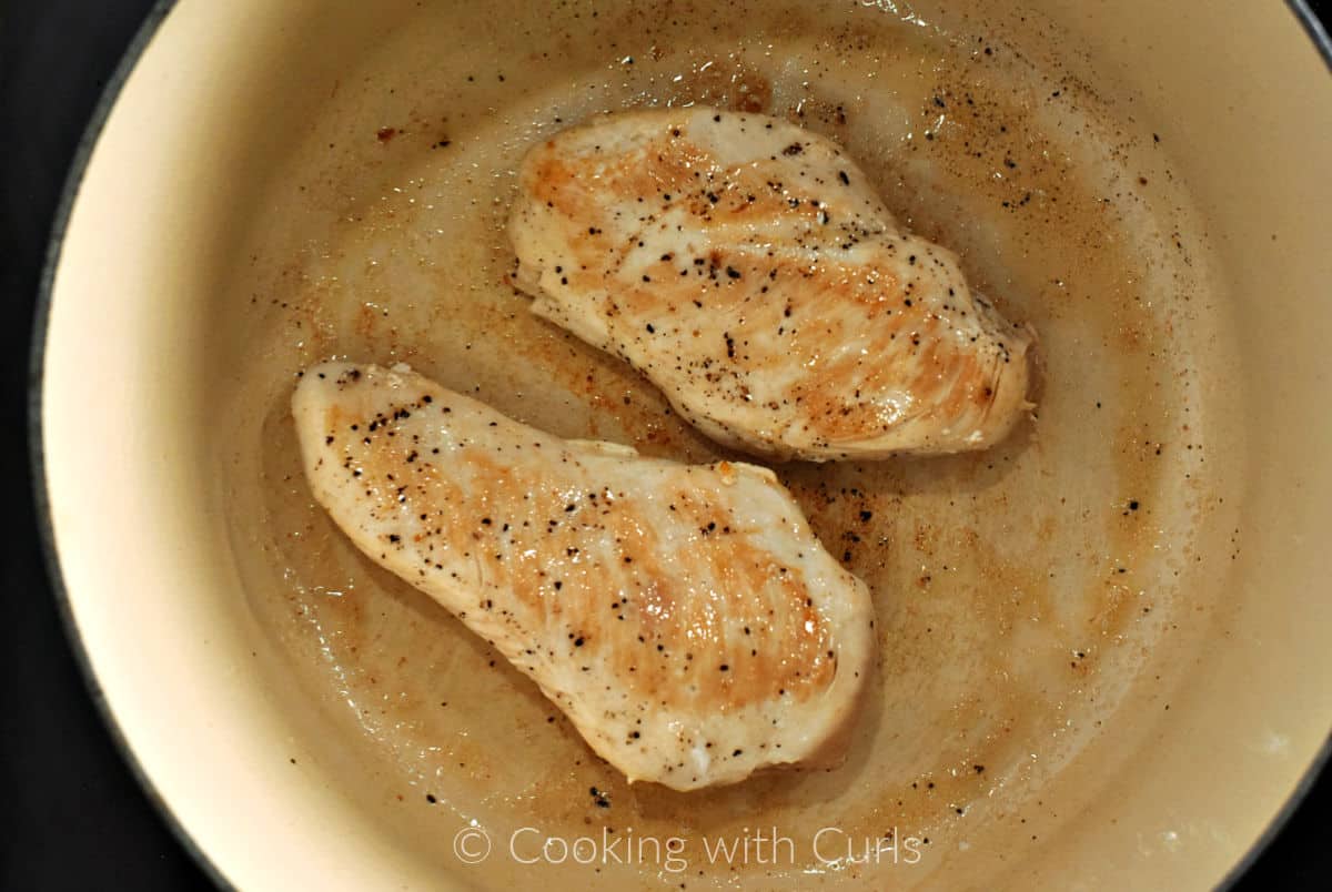 Two boneless chicken breasts seared in oil in a pan. 