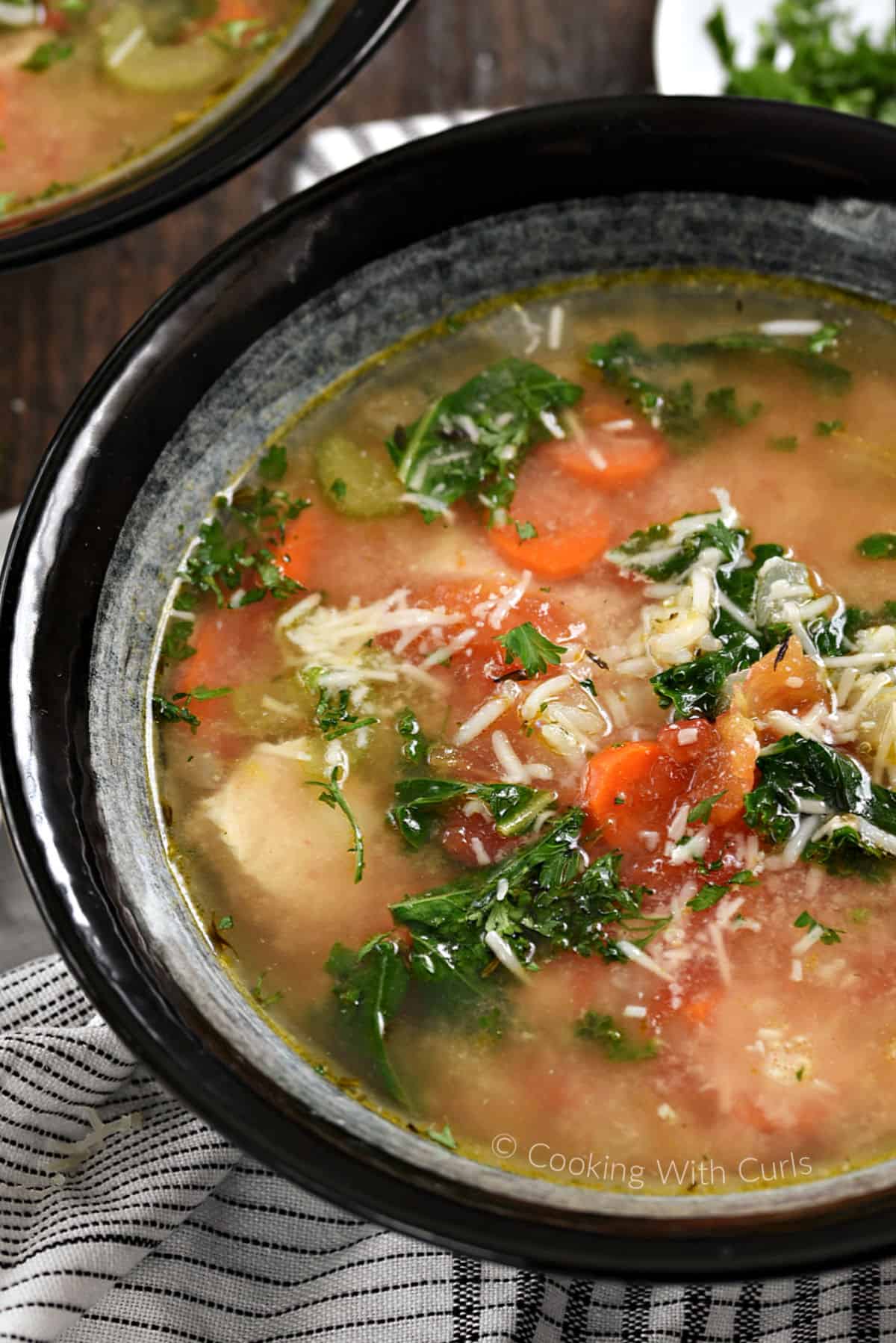 A big bowl of chunky chicken soup with carrots, celery, kale, and grated parmesan. 