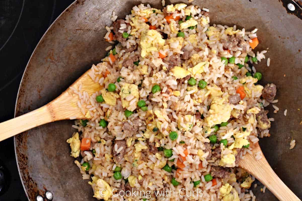 Breakfast Fried Rice with sausage, scrambled eggs, peas and carrots in a wok with two bamboo turners. 