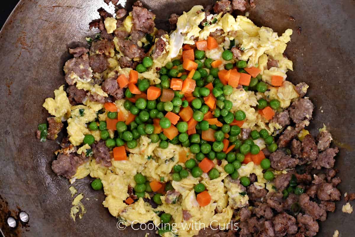 Diced carrots and peas on top of scrambled eggs and sausage in a wok. 
