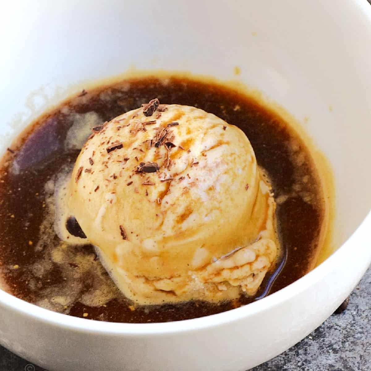 A scoop of ice cream in a white bowl topped with espresso and chocolate shavings.