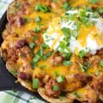 potato rounds topped with chili, cheddar cheese and a serving of sour cream in the center presented in a cast iron skillet sitting on a green plaid napkin