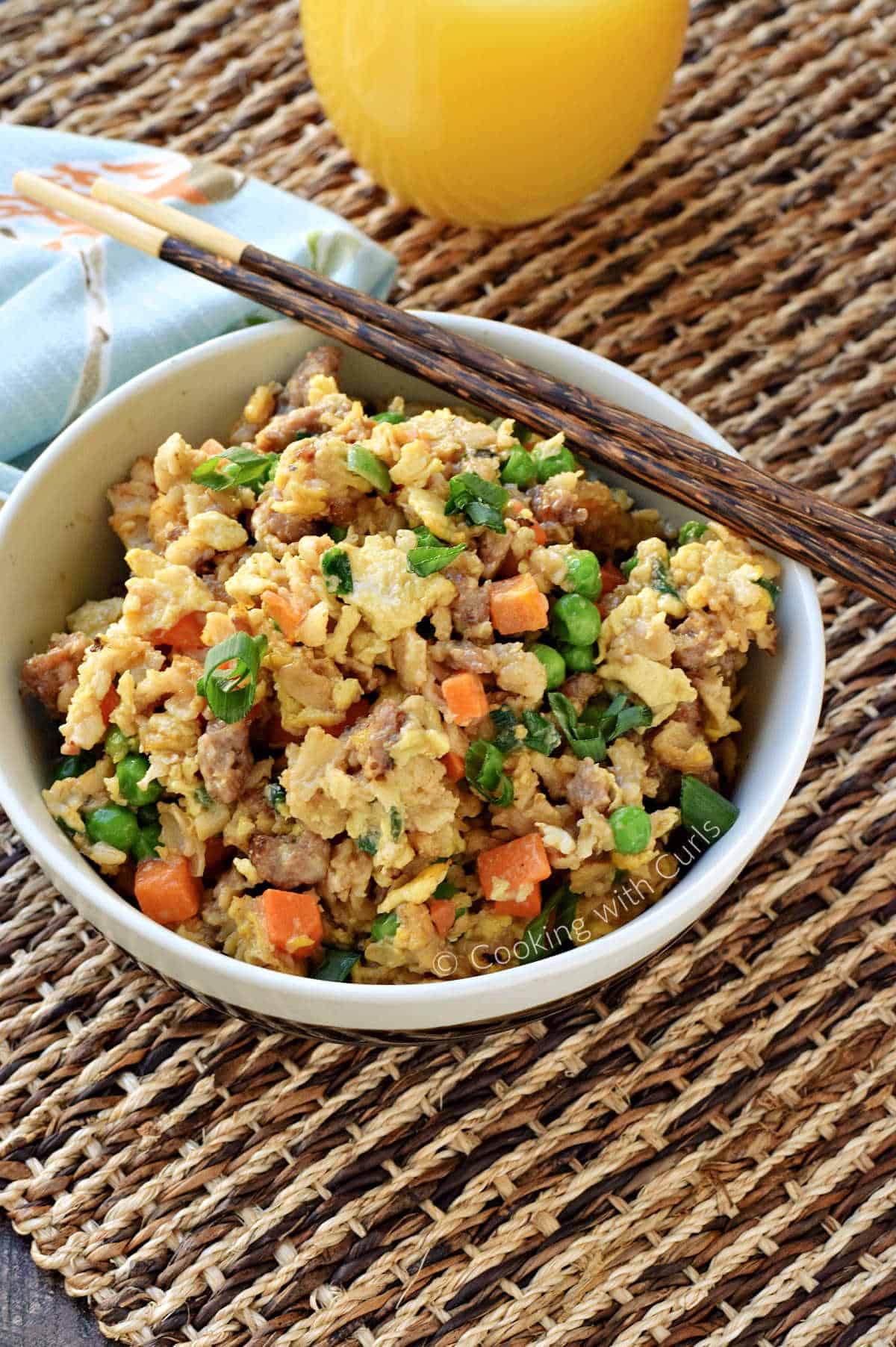 Scrambled eggs, pork sausage, peas, carrots, cooked oatmeal and green onions in a bowl with chopstick laying on the edge. 
